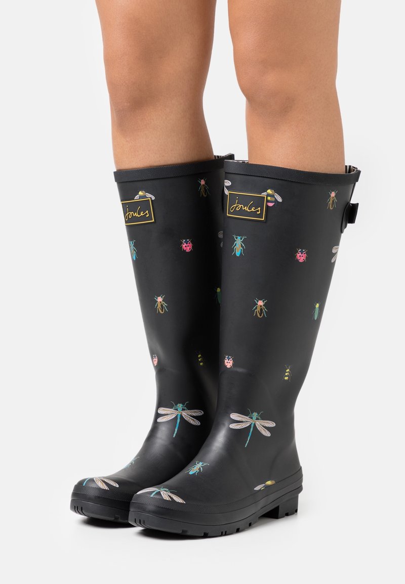 Bottes de pluie en caoutchouc noir ornées de motifs d'insectes colorés, comprenant des coccinelles et des libellules, avec une étiquette de marque et des semelles texturées.