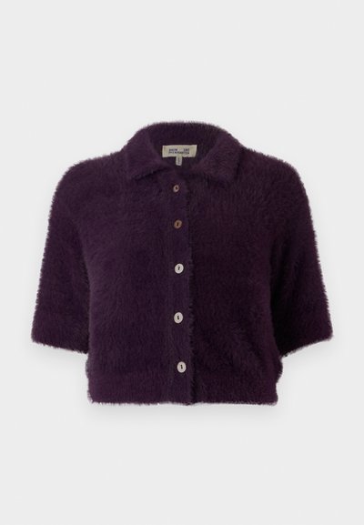 Fioletowy, puszysty sweter z krótkim rękawem, z przodu zapinany na guziki oraz z kołnierzykiem. Posiada drewniane guziki i miękką teksturę.