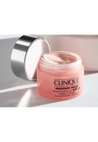 Pot rose de Clinique Moisture Surge avec une crème lisse à l'intérieur, couvercle argenté, étiqueté avec les détails du produit et les informations SPF.