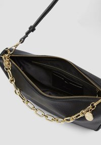 Schwarze Lederhandtasche mit strukturiertem Finish, goldener Kettenakzent, Reißverschluss und Innentasche. Gefüttert mit dunklem Stoff.