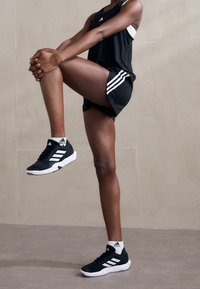 Svarta sportskor med vita detaljer, inklusive tre ränder, kombinerade med svarta shorts och en svart linne, har en sportig design.