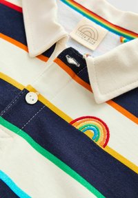 Polohemd mit cremefarbenen, marineblauen und bunten Streifen. Es hat einen Knopfverschluss und ein gesticktes Regenbogen-Design auf der Vorderseite.
