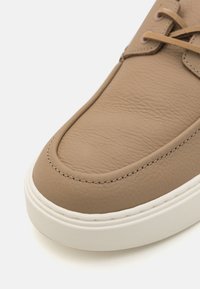 Sneaker in pelle color tan con una texture liscia, punta arrotondata, suola in gomma bianca e dettagli cuciti lungo il bordo. Design con lacci.