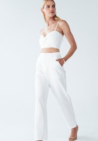 Biały krótki top z skręconym przodem, w parze z szerokimi białymi spodniami. Gładki materiał i minimalistyczne akcenty.