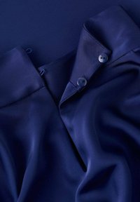 Tissu de chemise bleu marine avec une texture lisse, présentant un col, deux boutons et des détails en boucle sur l'encolure.