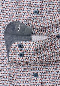 Herrenhemd mit einem farbenfrohen geometrischen Muster in Blau, Rot und Beige; verfügt über blaue Knöpfe und einen kontrastierenden dunklen Manschette mit Stichdetails.