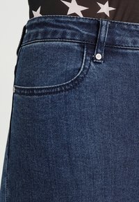 Tmavě modré džíny z denimu s klasickým designem pěti kapes, s detailním nýtovacím uzávěrem a hladkou texturou.