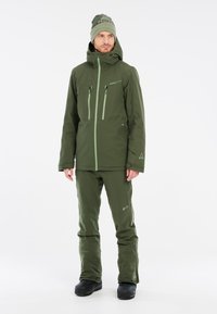 Grüne Outdoor-Jacke mit passenden Hosen, ausgestattet mit Reißverschlusstaschen und einer taillierten Kapuze, aus einem strukturierten, wasserabweisenden Material gefertigt.