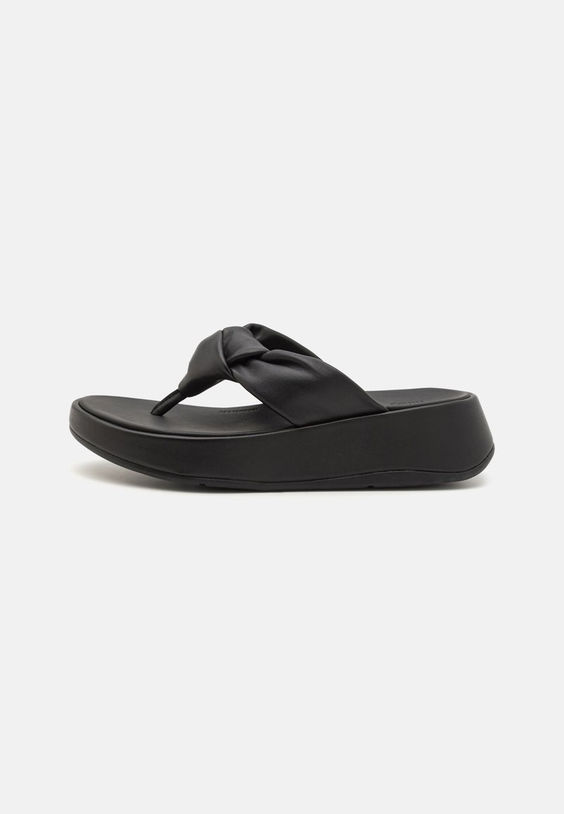 Musta flip-flop-sandaali, jossa on solmittu nahkaremmi, muotoiltu pohja ja paksu, pehmustettu pohja lisäkorkeutta ja mukavuutta varten.