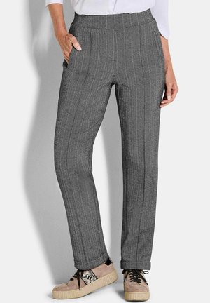 Femme portant un pantalon droit gris à motif chevrons avec taille élastique et des baskets beiges à lacets, debout avec une main dans la poche.