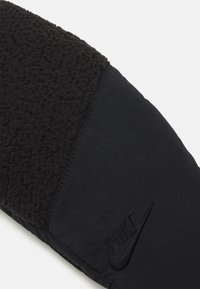 Black sneaker featuring a textured fleece upper and smooth fabric side panel, accented with an embossed Nike logo.