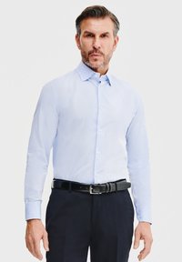 Jasnoniebieska koszula z długim rękawem, z klasycznym kołnierzykiem i prostym krojem, w połączeniu z ciemnymi spodniami i czarnym paskiem.