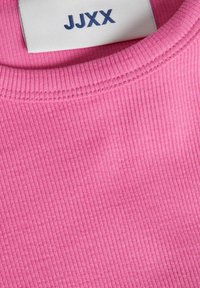 Rosa ribbad tyg av en T-shirt med rund halsringning och etikett med "JJXX" i blått. Texturen verkar mjuk och lätt.