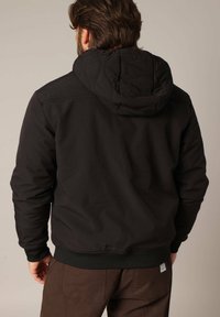 Zwarte hoodie met een gewatteerde capuchon, geribbelde manchetten en zoom. De stof lijkt soepel en duurzaam, met een minimalistisch ontwerp.