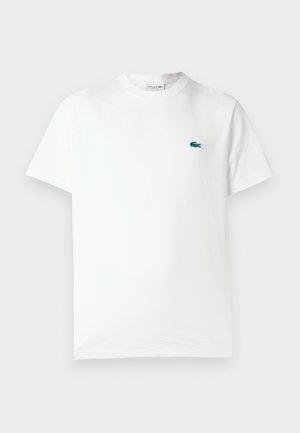 Camiseta de algodón blanca con cuello redondo, mangas cortas y un pequeño logo de cocodrilo bordado en verde en el lado izquierdo del pecho.