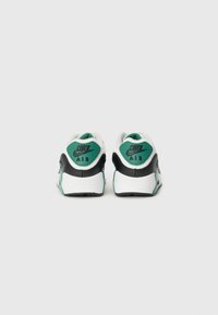 Nike Air tenisky majú biely a čierny zvršok s zelenými akcentmi, textúrovaný opätok a výrazné logo na zadnej strane.