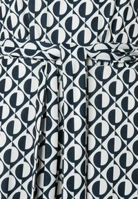 Een stoffen riem met een herhalend geometrisch patroon van donkerblauwe en witte cirkels en kwartcirkels, met een gladde textuur.