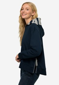 Mörkblå hoodie med en kontrasterande mönstrad huva, åtsittande muddar och sidofarvor. Tillverkad av mjukt material och med en avslappnad siluett.