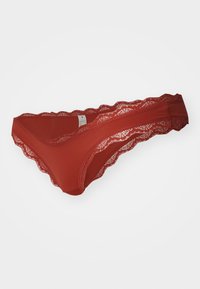 Red lace thong with scalloped edges, featuring a smooth waistband and lightweight fabric. Intricate pattern along the lace detailing.