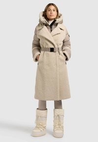 Sāls krāsas divrindu mētelis ar kažokādas līdzīgu tekstūru, polsterētām piedurknēm un jostu jostasvietā. Apvienots ar krēmkrāsas ziemas zābakiem.