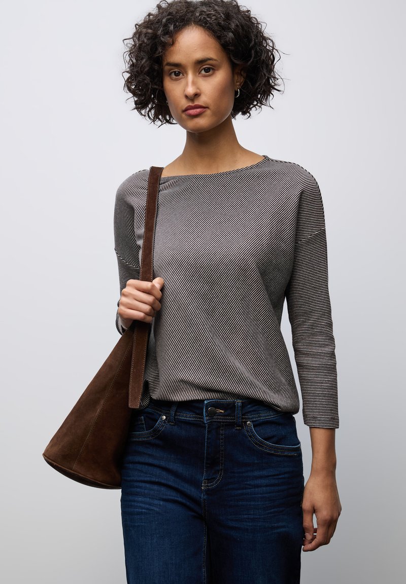 Grårandig långärmad topp i kombination med mörkblå jeans. Modellen håller en brun mockatotepåse. En enkel ljus bakgrund.