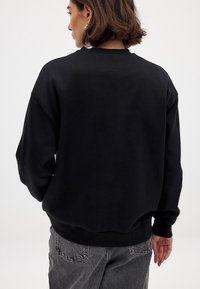 Zwarte sweatshirt met een ronde halslijn en geribde manchetten. Gemaakt van zachte stof, met verlaagde schouders en een ontspannen pasvorm.