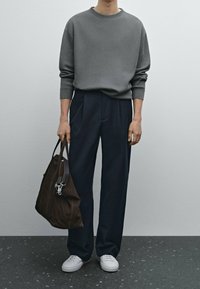 Grau gerippter Pullover, marineblaue hochtaillierte Hose, weiße Sneakers und eine braune Lederhandtasche mit silbernen Details. Glatte Textur und lockere Passform.