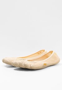 Beiga nätbalettkor med öppen vävdesign, rund tå, flexibel sula och gula detaljer på hälen. Passar för varmt väder.