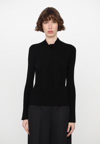 Black ribbed sweater with long sleeves and a bow tie detail at the neck. The material appears smooth and fitted, with a delicate texture.