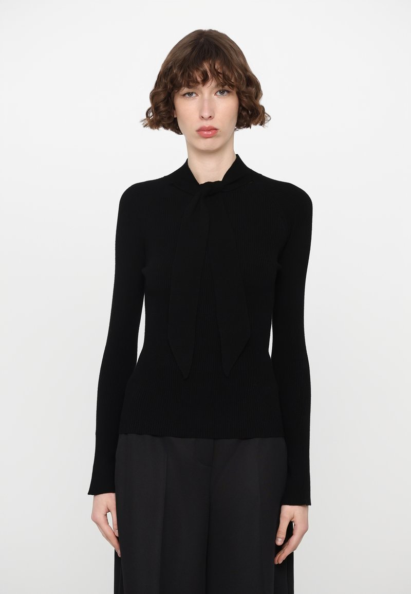 Black ribbed sweater with long sleeves and a bow tie detail at the neck. The material appears smooth and fitted, with a delicate texture.