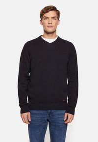 Pulover negru cu decolteu în V și mâneci lungi, cu manșete și tiv cu dantelă. Fabricat dintr-un material moale, asortat cu blugi albaștri. Design minimalist.