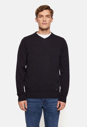 Zwarte v-hals trui met lange mouwen, geribde manchetten en zoom. Gemaakt van een zachte stof, gedragen met blauwe jeans. Minimalistisch ontwerp.