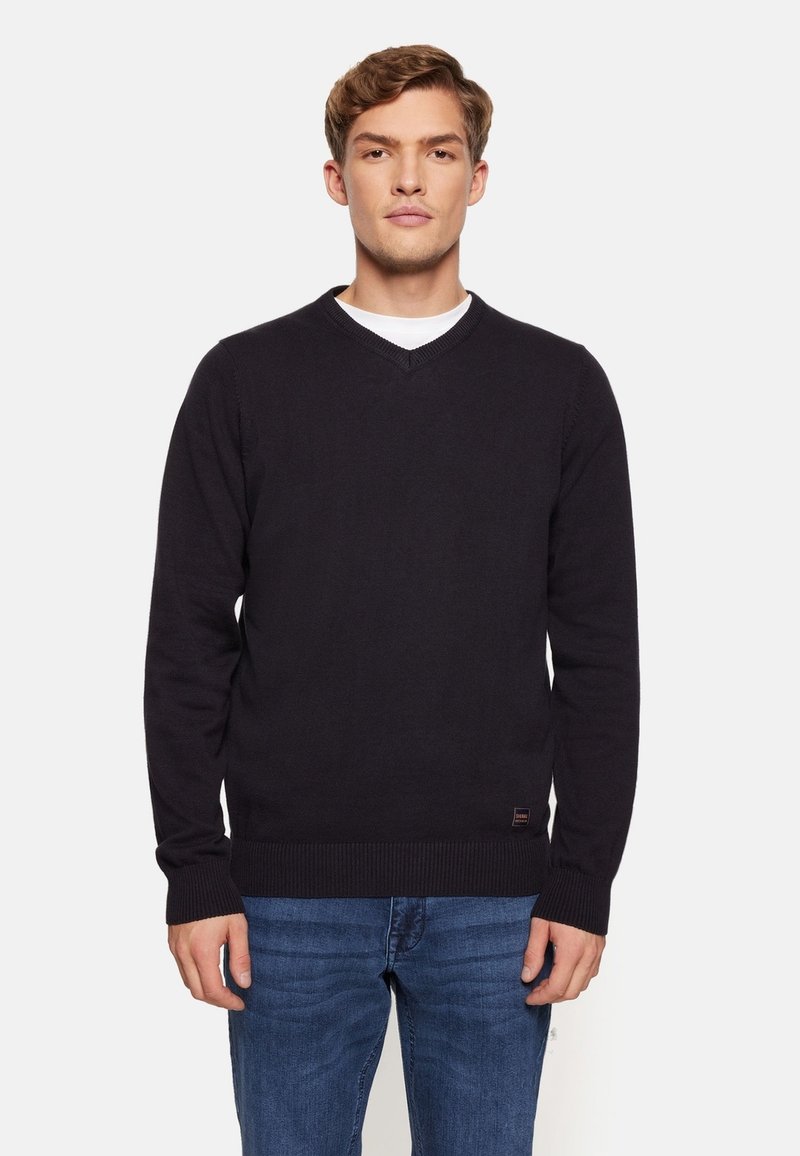 Pulover negru cu decolteu în V și mâneci lungi, cu manșete și tiv cu dantelă. Fabricat dintr-un material moale, asortat cu blugi albaștri. Design minimalist.