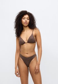 Καφέ σετ μπικίνι με τριγωνικό τοπ με διακοσμητικές οπές σε σχήμα τελειωμάτων και λεπτές τιράντες, συνοδευόμενο από σλιπ με ψηλή μέση και παρόμοιες λεπτομέρειες.