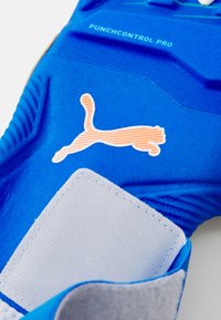 Blå målvakthandske med texturerat grepp, grå patch och orange Puma-logotyp. Materialet är syntetiskt, designat för ökad kontroll och skydd.