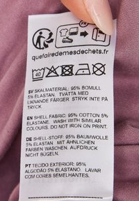 Etykieta z instrukcją prania; zawartość tkaniny: 95% bawełna, 5% elastan. Szare tło z czarnym tekstem; obecne różne języki.