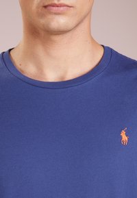 Kungligt blå kortärmad t-shirt i bomull med rund halsringning och en liten orange polo-logotyp på vänster bröst.