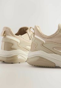Beżowe buty sportowe z siateczkową cholewką, gładkimi syntetycznymi wstawkami, wyściełanym kołnierzem i teksturowaną podeszwą. Ciekawie zaprojektowane akcenty po bokach.