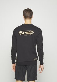 Felpa nera con logo dorato "KING" sul retro, polsini e orlo a coste, con un fit casual, abbinata a pantaloni corti neri.
