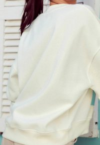 Cream-colored sweatshirt with a relaxed fit, featuring a soft, textured fabric, ribbed cuffs, and a round neckline.