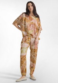 To-delt sæt i brun, bladmønstret stof med løse, brede ærmer og elastiske manchetter på bukserne. Letvægts og farverigt design.
