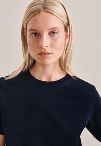 Granatowa bawełniana koszulka z okrągłym dekoltem i krótkimi rękawami, charakteryzująca się gładką teksturą i minimalistycznym wzornictwem.