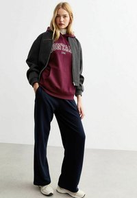Felpa bordeaux con la scritta "MONTANA USA", indossata sotto una giacca bomber grigia cropped. Abbinata a pantaloni blu larghi e sneakers beige.