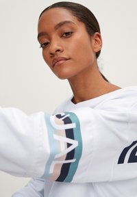 Witte sweatshirt met kleurrijke strepen en tekstaccenten op de arm. De stof ziet er zacht uit en heeft een relaxte pasvorm en capuchonontwerp.