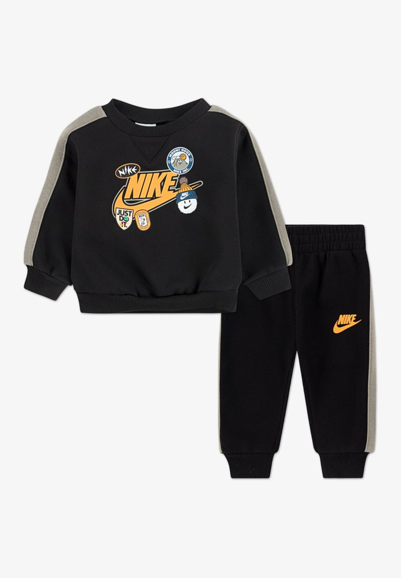 Crni set dukserice i hlača s narančastim Nike logotipom. Ima sive akcentne detalje i razne zakrpe na dukserici. Mekana, rastezljiva tkanina.