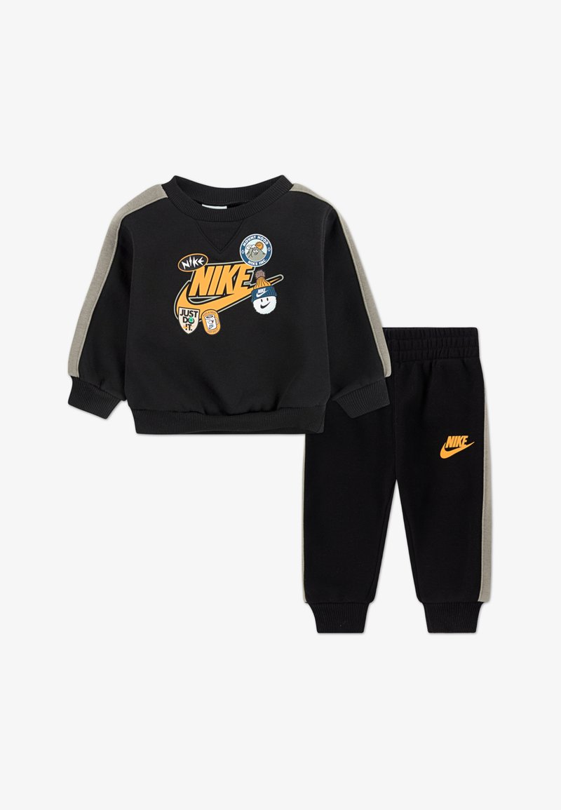 Melnas sporta krekliņš un bikses komplekts ar oranžu Nike logo. Iezīmēts ar pelēkiem akcentiem un dažādām uzlīmēm uz krekliņa. Gluda, elastīga auduma.