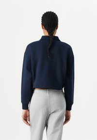 Mørkeblå kort sweatshirt med høy krage og ribbestrikkede mansjetter, kombinert med lysegrå joggebukser. Glatt stoff, avslappet passform.