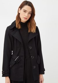 Abrigo negro con un amplio cuello, cierre de botones, detalles de cinturón y bolsillos laterales. Tela suave con un corte entallado.