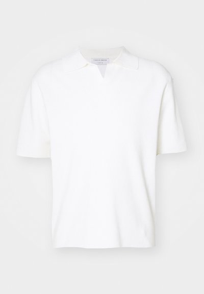 Fehér, rövid ujjú pólóing, galléros nyakkal és finom v-alakú hasítékkal. Puha anyagból készült, sima textúrával.
