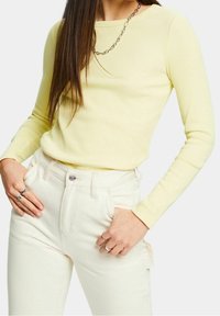 Haut à manches longues en ribbed de couleur jaune pastel doux, associé à un jean blanc taille haute. Il présente un col rond simple et une silhouette ajustée.